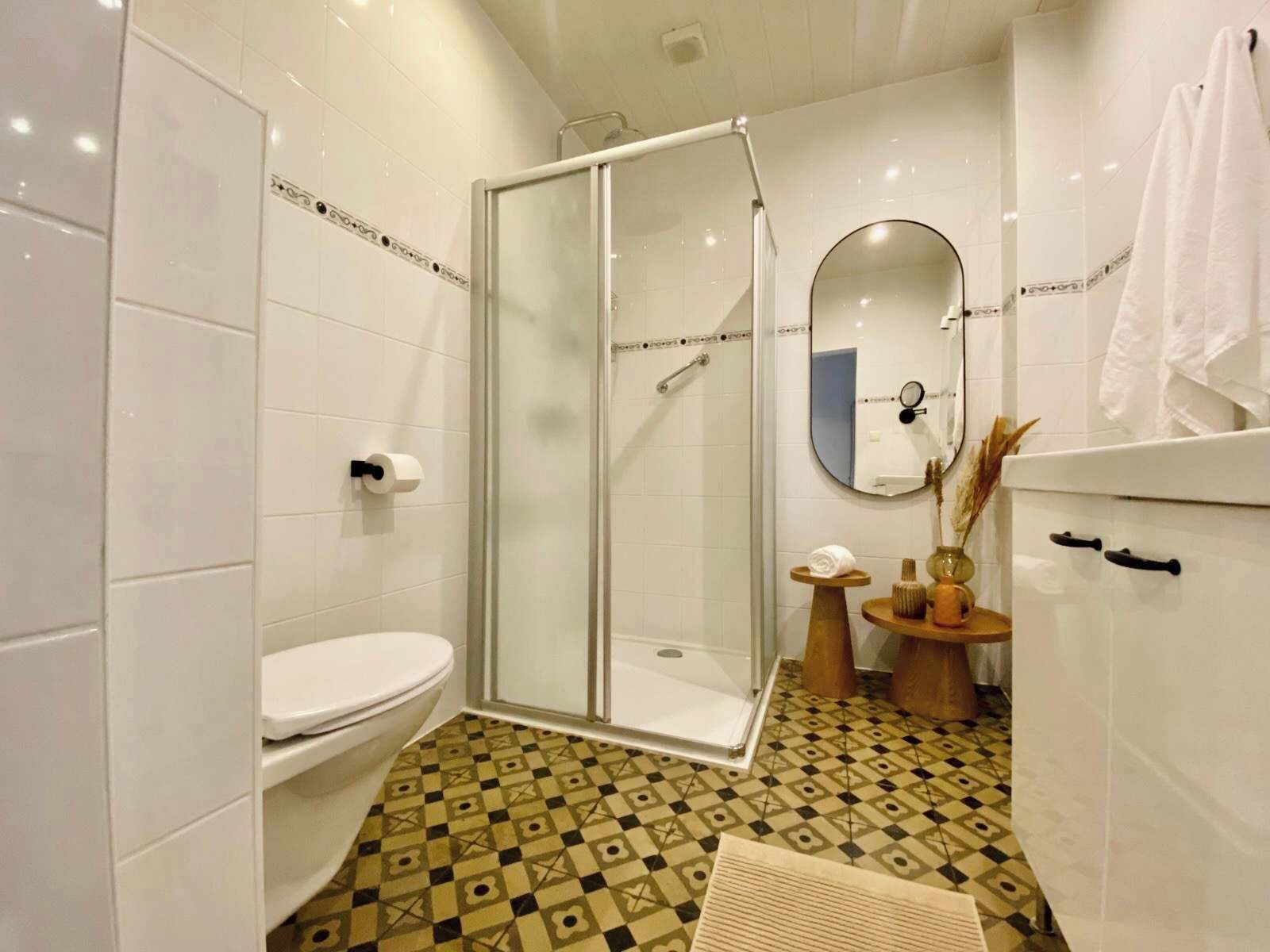 Een badkamer met een douche met glazen wand, een toilet, een wastafel met spiegel en een vloer met patroon.
