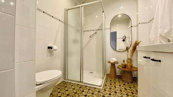 Een badkamer met een douche met glazen wand, een toilet, een wastafel met spiegel en een vloer met patroon.