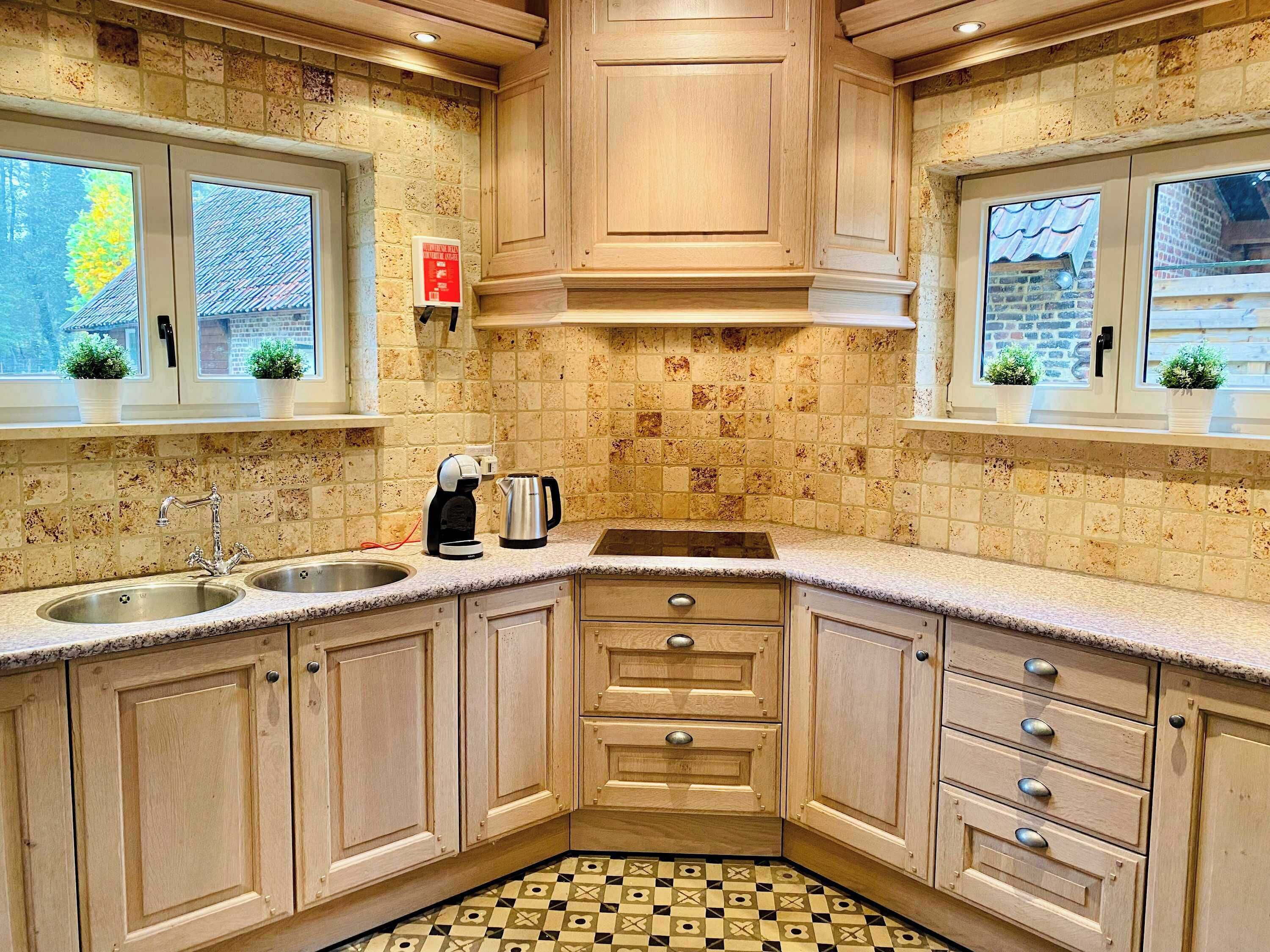 A kitchen with a double sink, a coffee maker, and a kettle. There are cabinets with drawers and a window with a view of the outside.