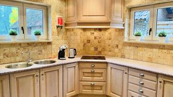 A kitchen with a double sink, a coffee maker, and a kettle. There are cabinets with drawers and a window with a view of the outside.