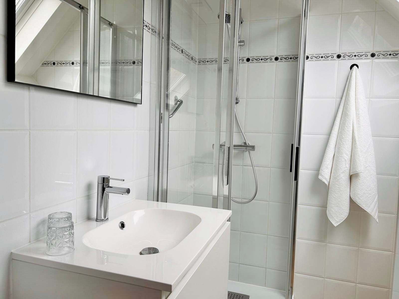 A modern bathroom with a glass-enclosed shower, a white sink, and a mirror above it.