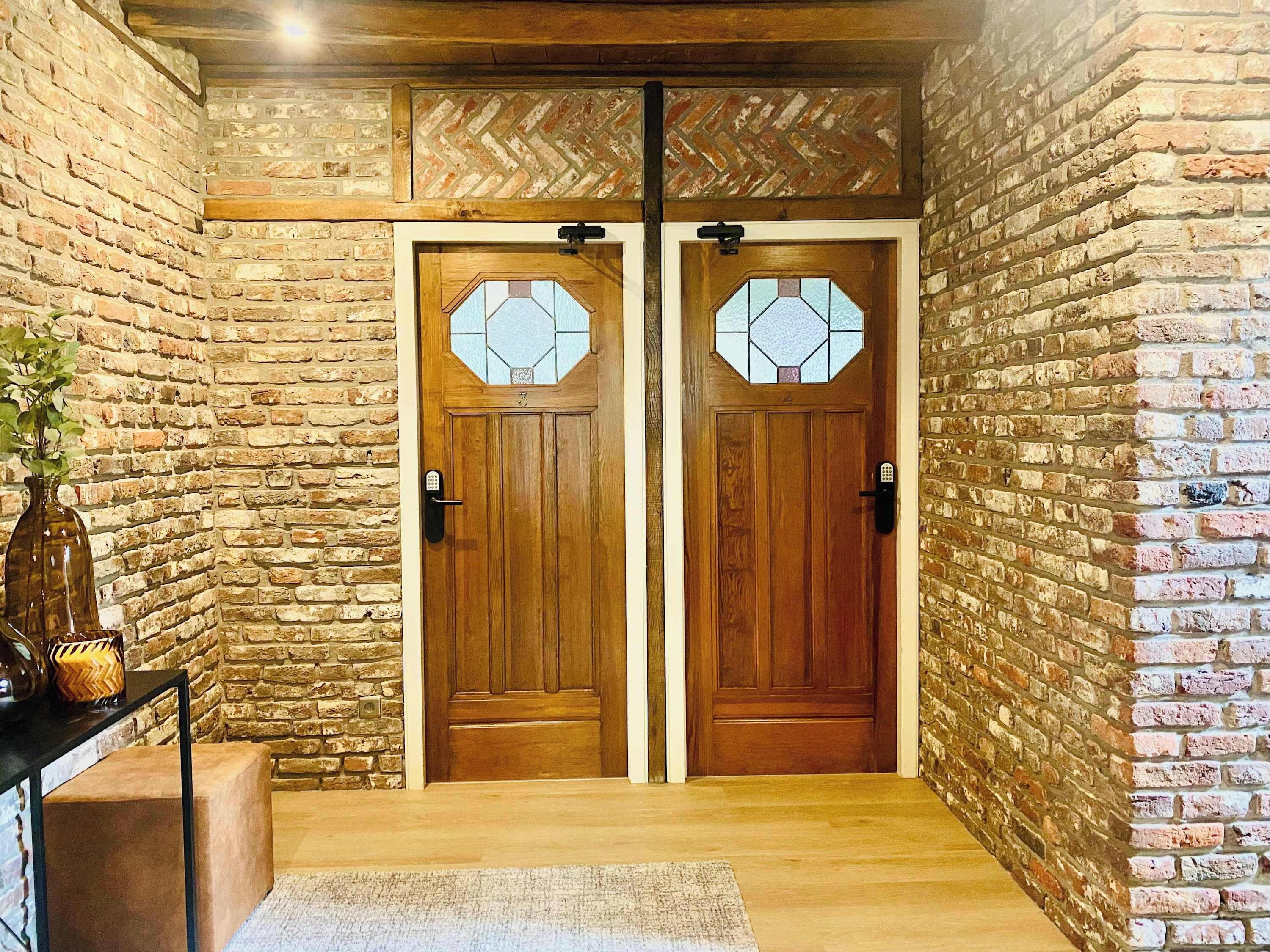 A wooden door with a glass panel and a keypad lock, set in a room with brick walls and a wooden floor.