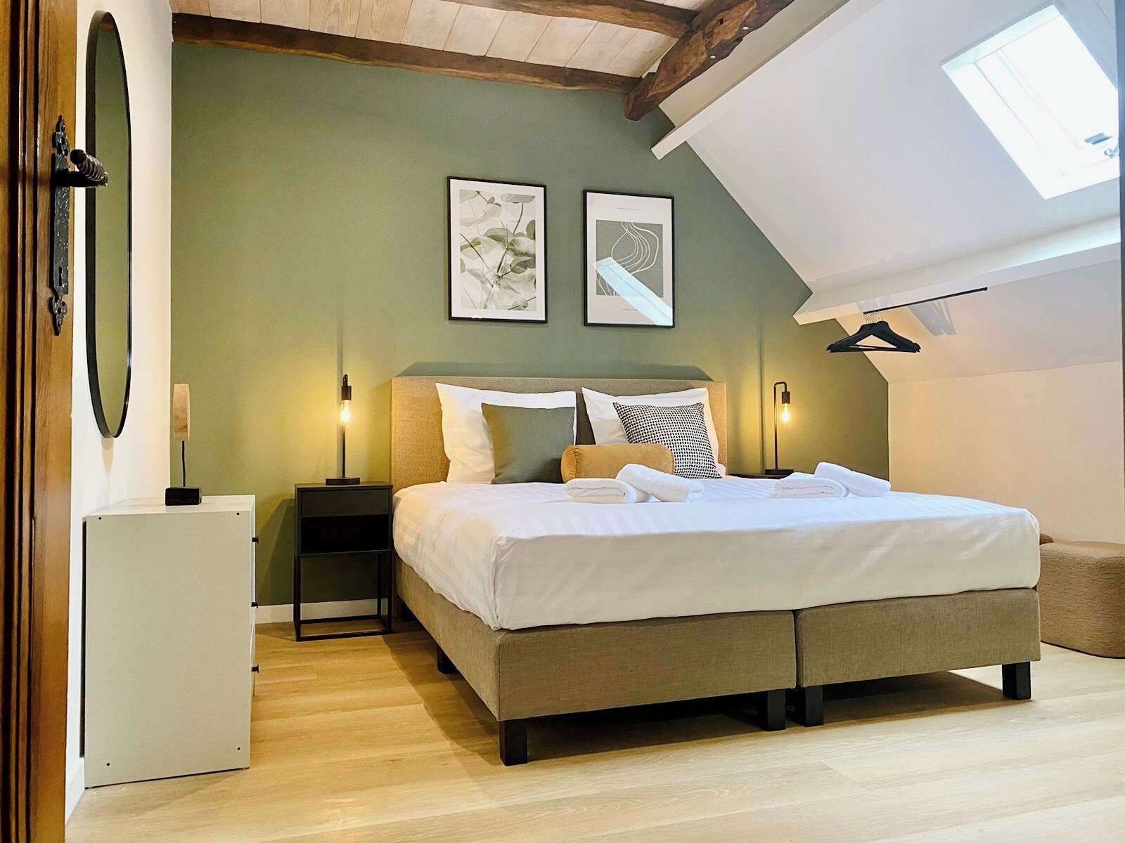 Un dormitorio con una cama, dos mesitas de noche, un espejo en la pared y dos cuadros enmarcados.