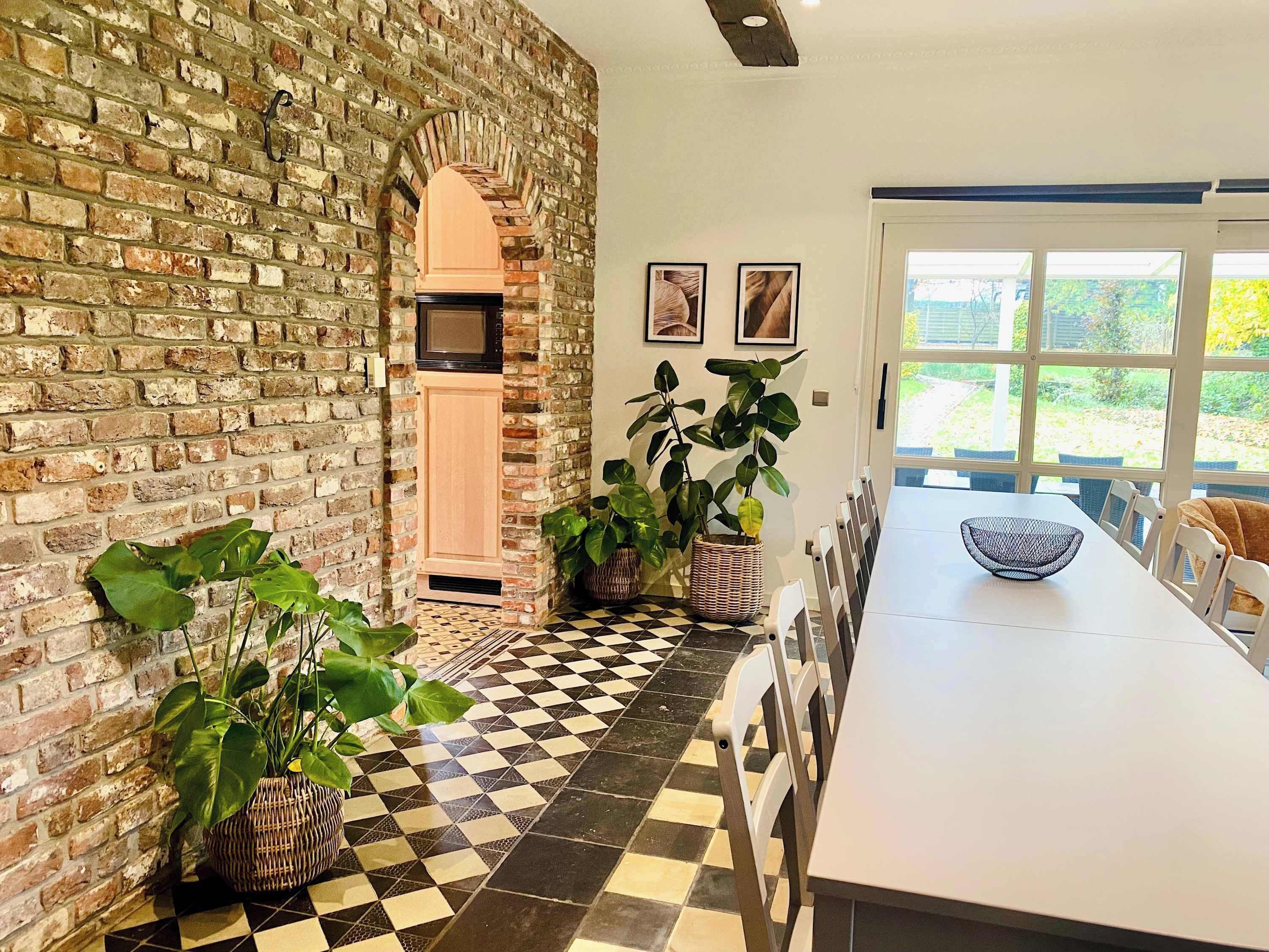 Un espace repas avec un mur en briques, un sol à carreaux et une grande fenêtre donnant sur un paysage verdoyant.