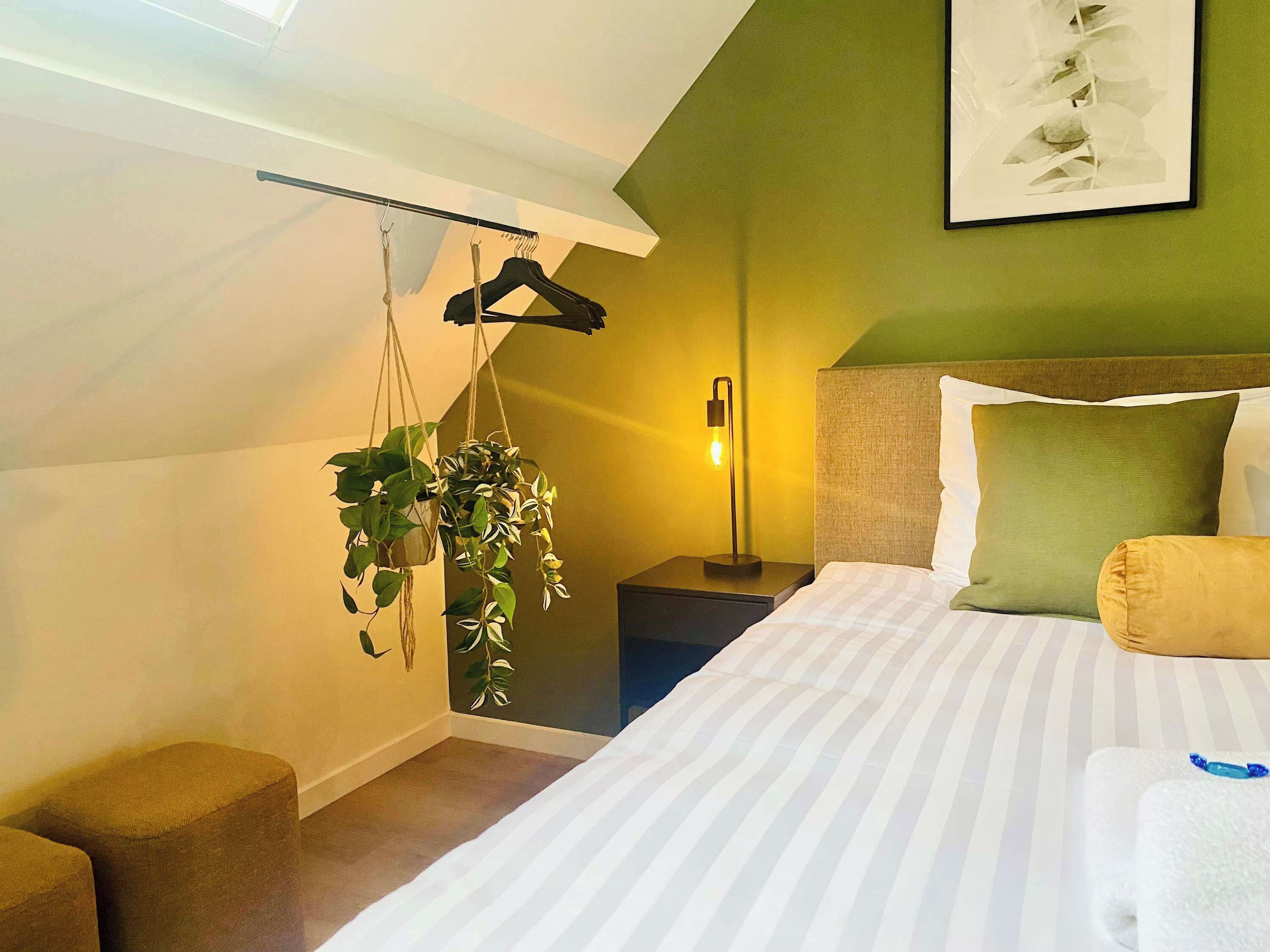 Un dormitorio con cama, una planta colgante, una mesita de noche y un buró.