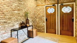Une pièce avec un mur en briques, des portes en bois ornées de vitraux, une console noire et deux tabourets rembourrés.