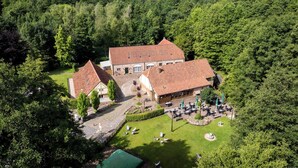 Un grand bâtiment coiffé d’un toit recouvert de tuiles rouges, entouré d’une végétation luxuriante et doté d’une pelouse bien entretenue avec des espaces de repos extérieurs.