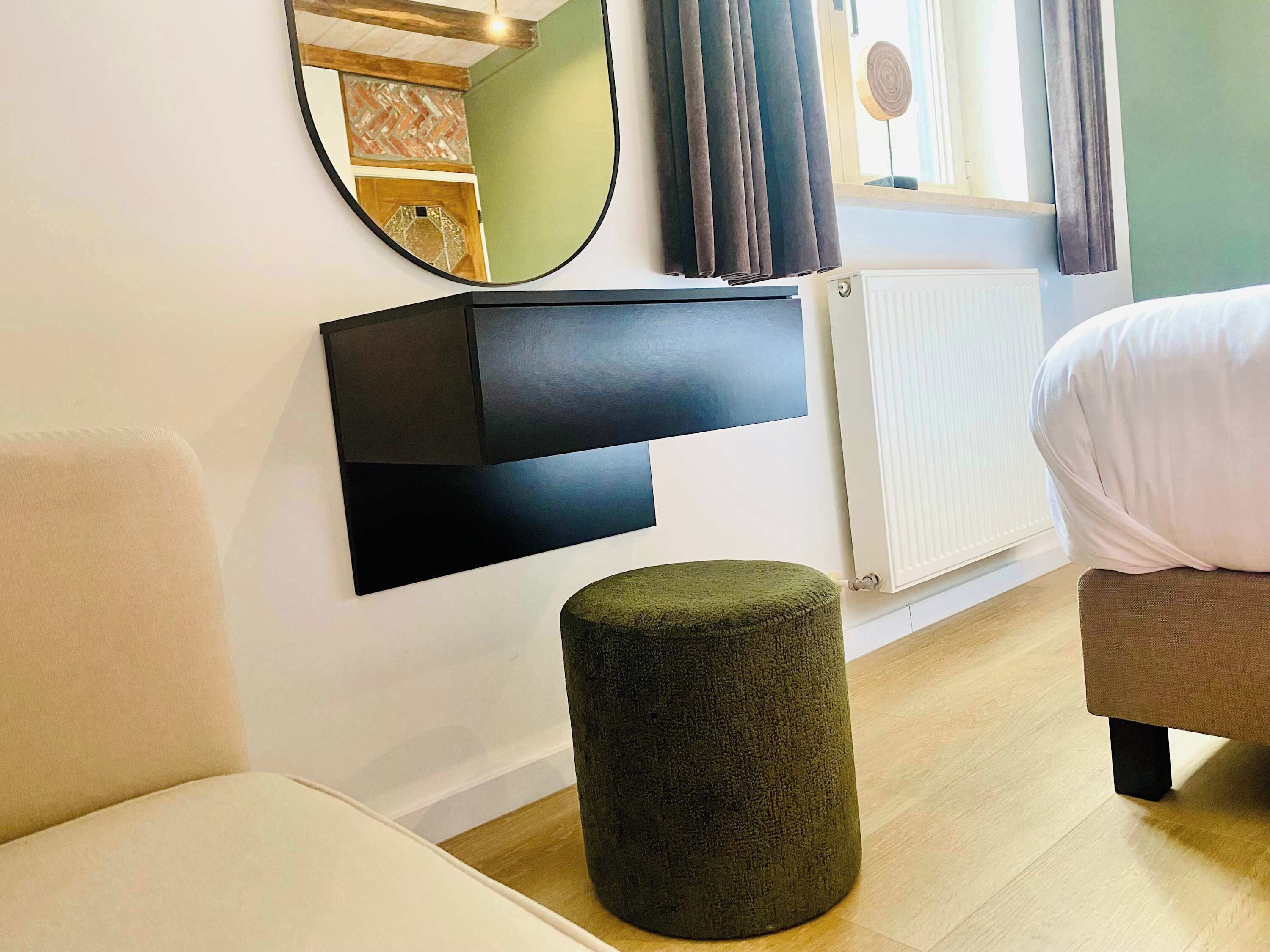 Ein modernes Zimmer mit einem runden Spiegel, einem schwarzen Regal, einem runden Hocker und einem Bett.