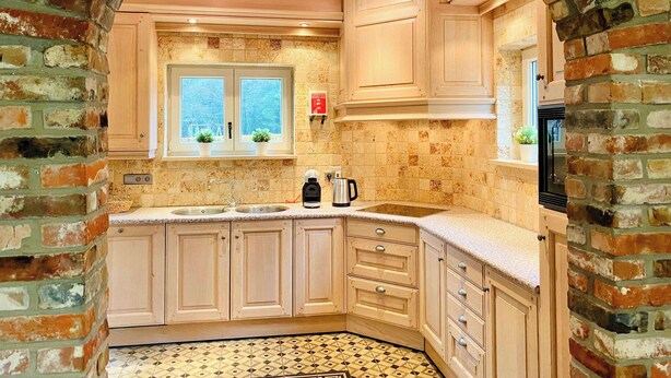 Une cuisine avec une arche en briques, des meubles en bois, un évier et une fenêtre ornée de plantes.