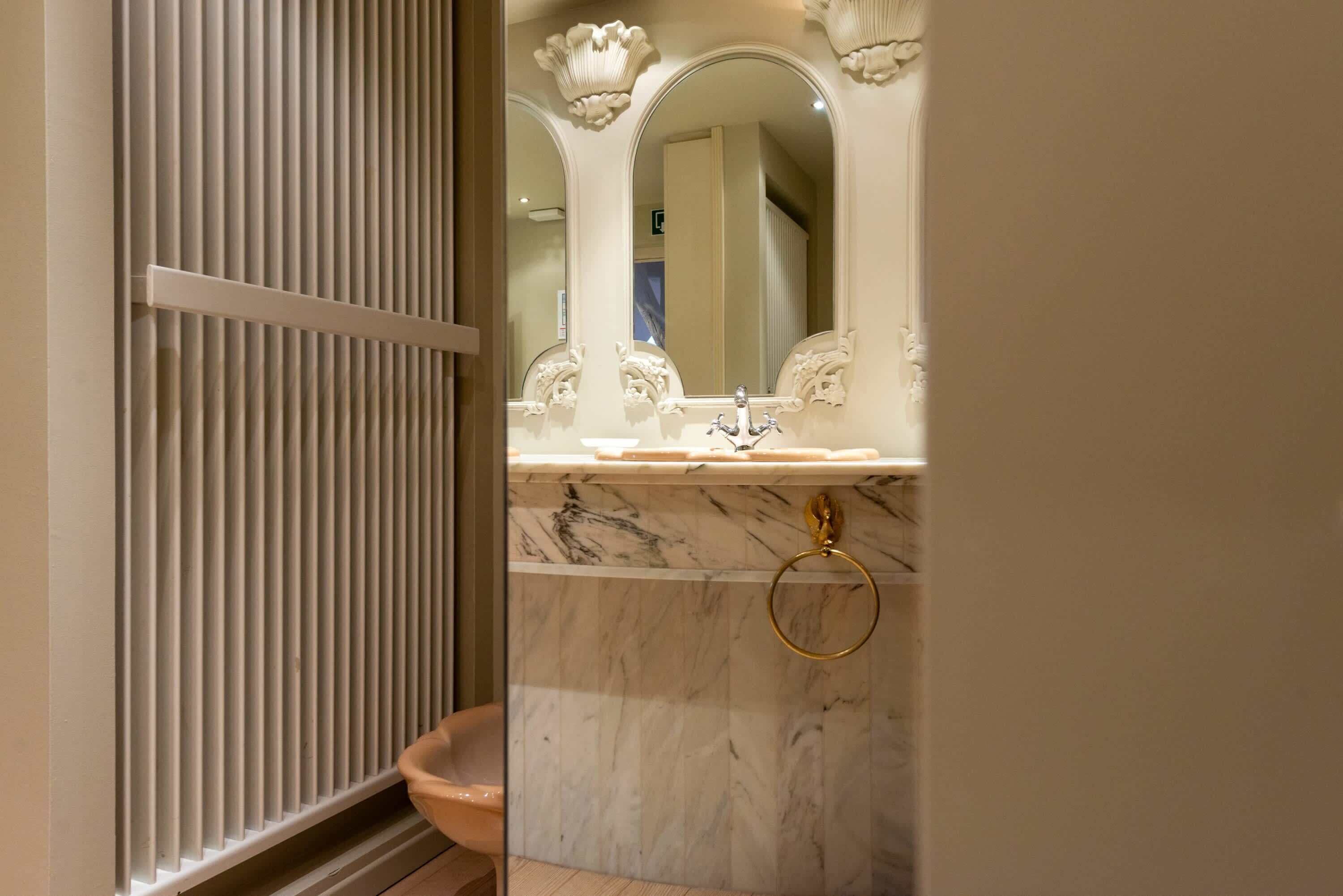 A bathroom with a marble sink, a gold towel ring, and a mirror with decorative elements.