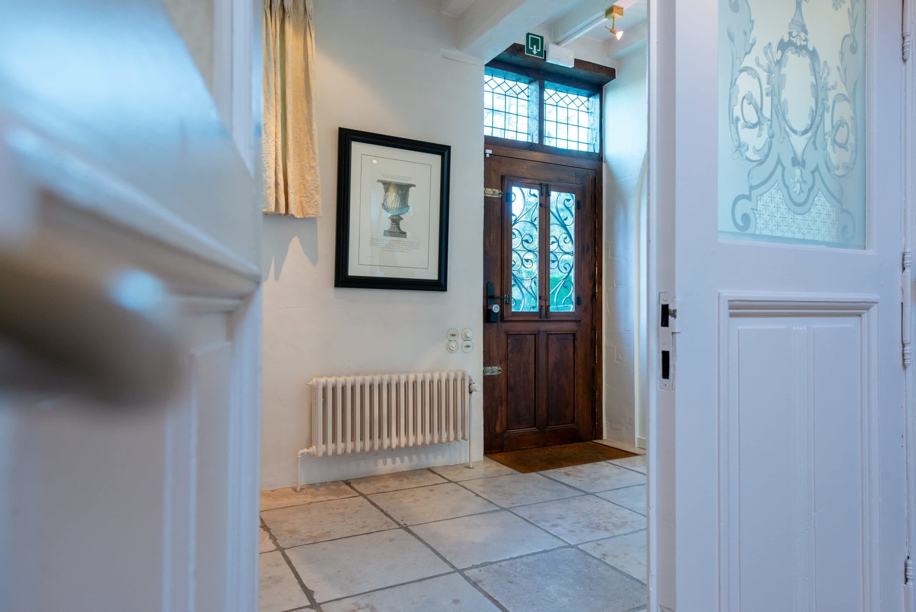 A hallway with a radiator, a framed picture on the wall, and a door with a glass window.
