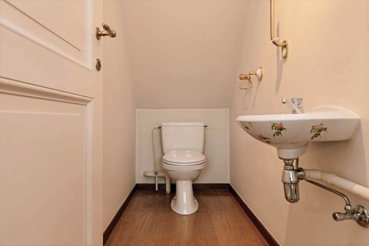 Ein kleines, kompaktes Badezimmer mit einer weißen Toilette, einem wandmontierten Waschbecken mit floralem Dekor und einem Holzboden.