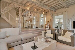 Amplia sala de estar con techo alto, vigas de madera a la vista, un candelabro y una escalera que conduce a un nivel superior.