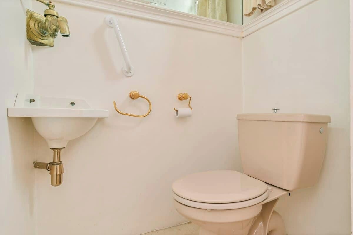 Un bagno con un lavandino bianco, un water e un rubinetto dorato.