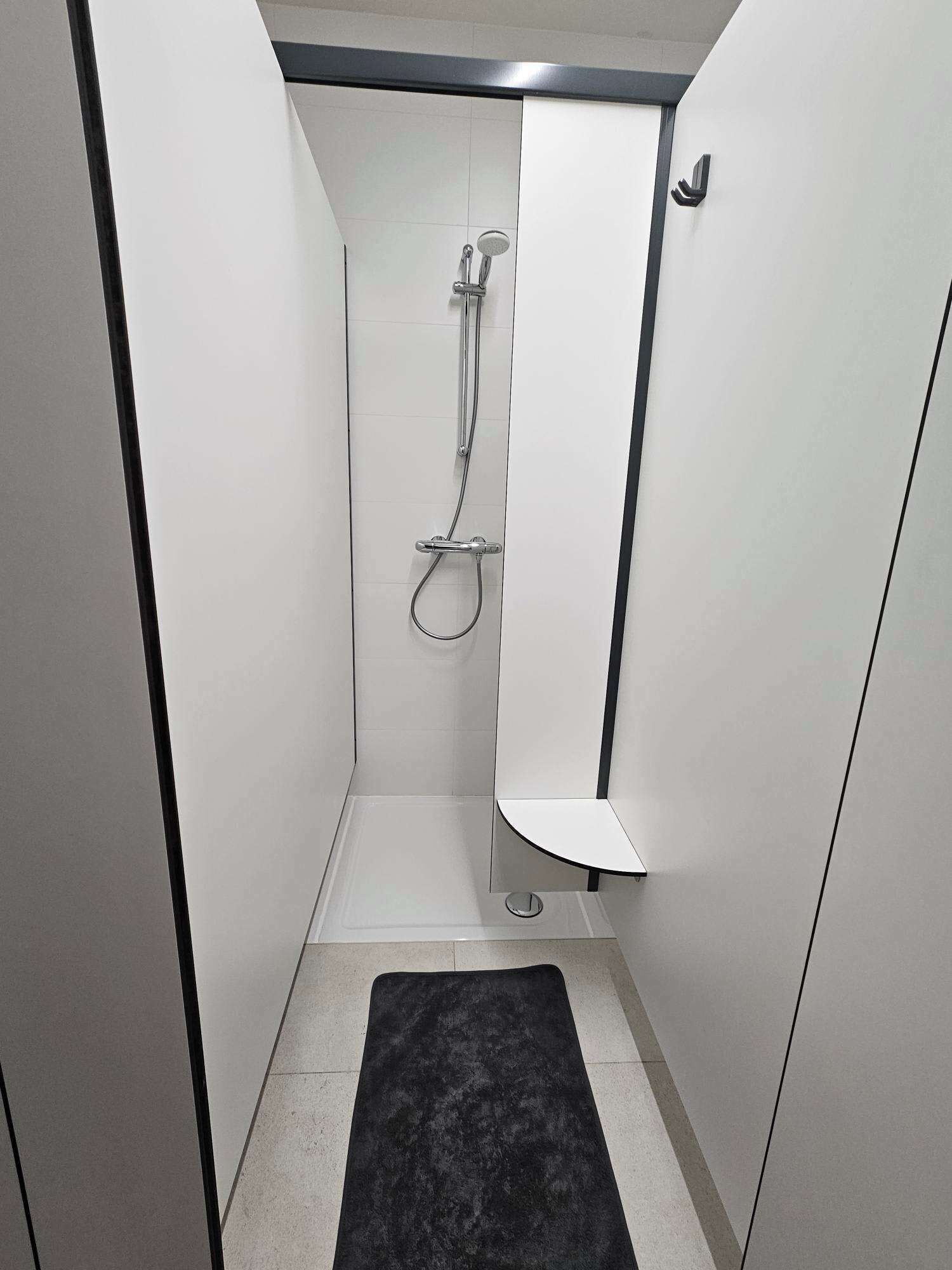 A narrow shower stall with a handheld showerhead and a wall-mounted faucet.