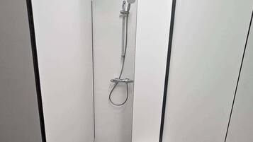 A narrow shower stall with a handheld showerhead and a wall-mounted faucet.