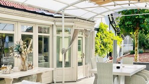 A covered outdoor seating area with wicker furniture and a glass enclosure.