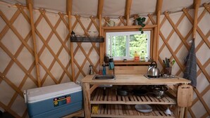 Een kleine keuken met een raam, houten planken en een koelbox.