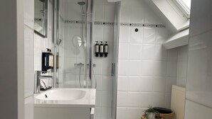 Ein modernes Badezimmer mit einer gläsernen Duschkabine, einem weißen Waschbecken und einem kleinen Holzschemel mit einer Pflanze.
