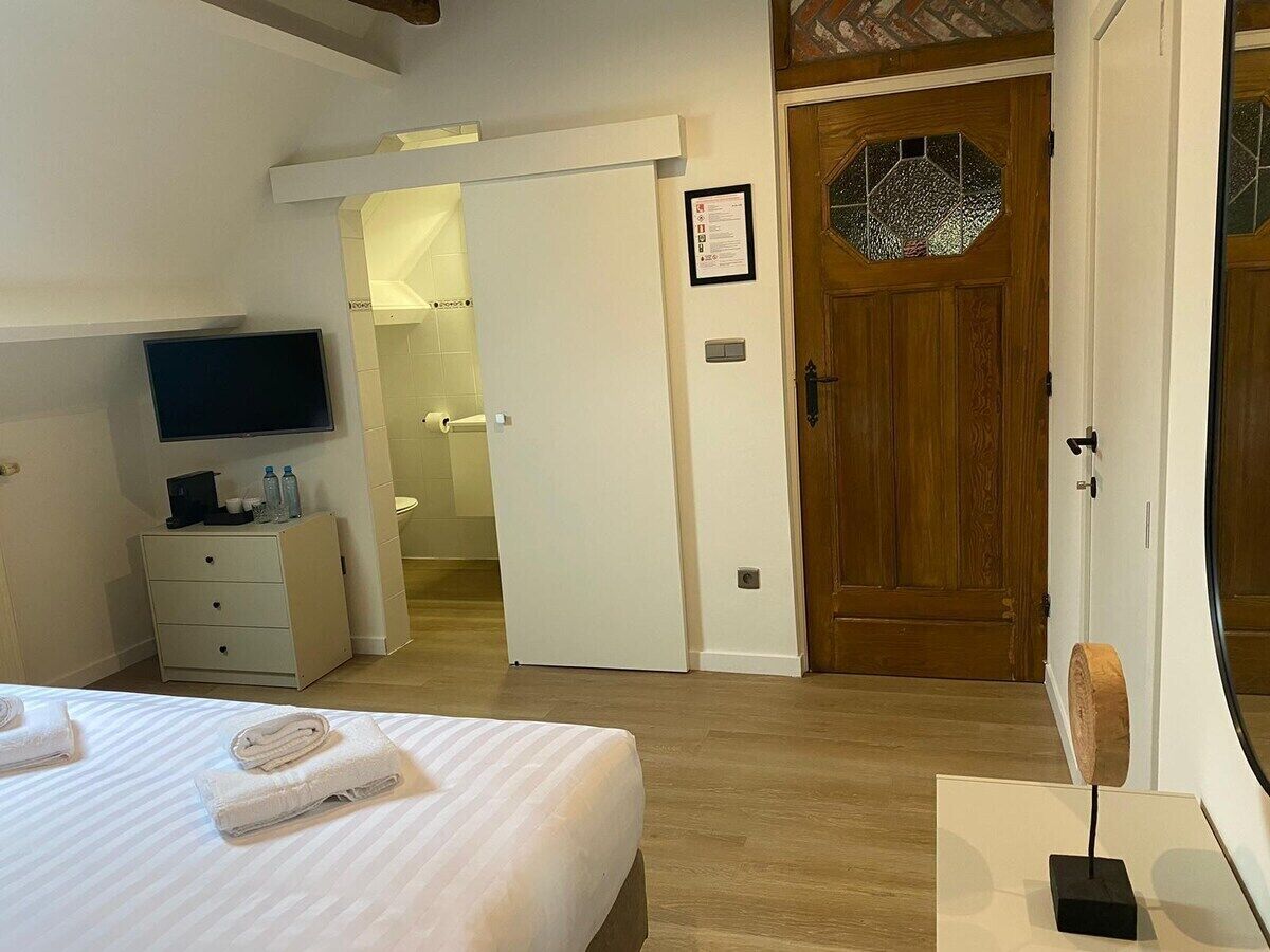 Hotelkamer met een bed, een televisie, een bureau met lamp, een houten deur en een zichtbare badkamer door een open deur.