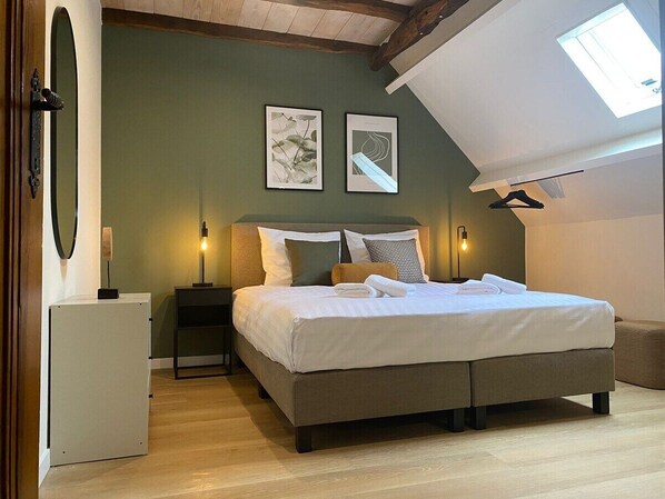 Un dormitorio con cama, mesitas de noche, un escritorio y un tragaluz.