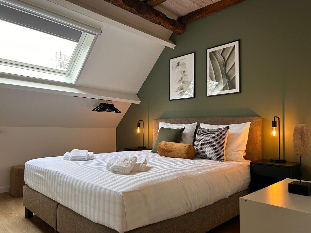 A bedroom with a skylight, a bed with white linens, two framed artworks, and bedside lamps.