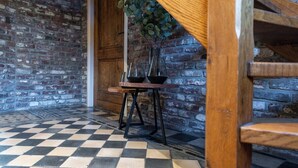 Un coin de pièce avec un sol à carreaux, une porte en bois et une table sur laquelle est posé un vase rempli de feuillage vert.
