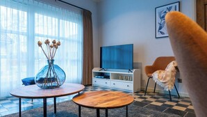 Un salon moderne avec une grande fenêtre, un téléviseur, une table basse et un fauteuil.