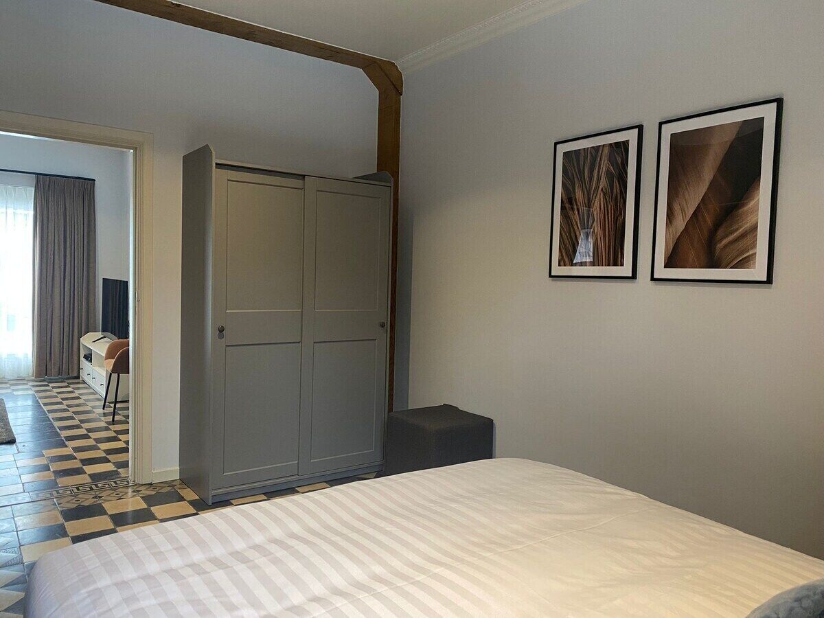 A hotel room with a bed, a wardrobe, a small table, and two framed pictures on the wall.