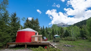A yurt with a red exterior, a solar panel, and a deck with chairs.