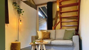 A cozy living room with a grey sofa, a small wooden side table, and a woven rug. - A1. De Fries: duplexsuite with terrace (Oudsbergen)