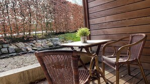A patio with a table and two wicker chairs, a potted plant, and a stone wall with a view of trees. - A1. De Fries: duplexsuite with terrace (Oudsbergen)