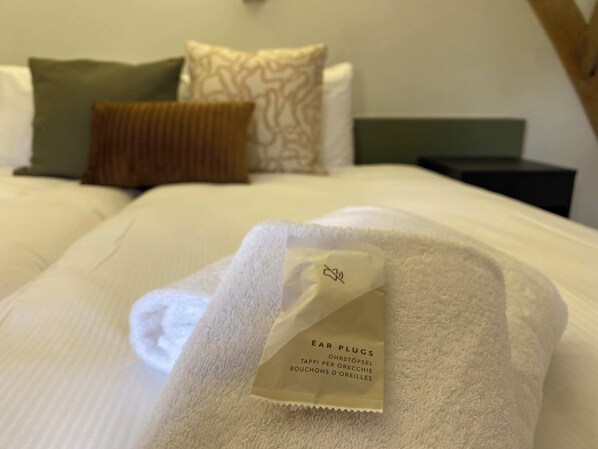 A neatly made bed with a white towel and a tag labeled "EAR PLUGS" on it.