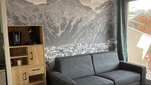 Un soggiorno con un divano grigio, una scaffalatura in legno e un murale raffigurante una montagna.