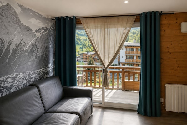 Una habitación con sofá de cuero, vista a un balcón con barandas de madera y un mural de paisaje montañoso en la pared.