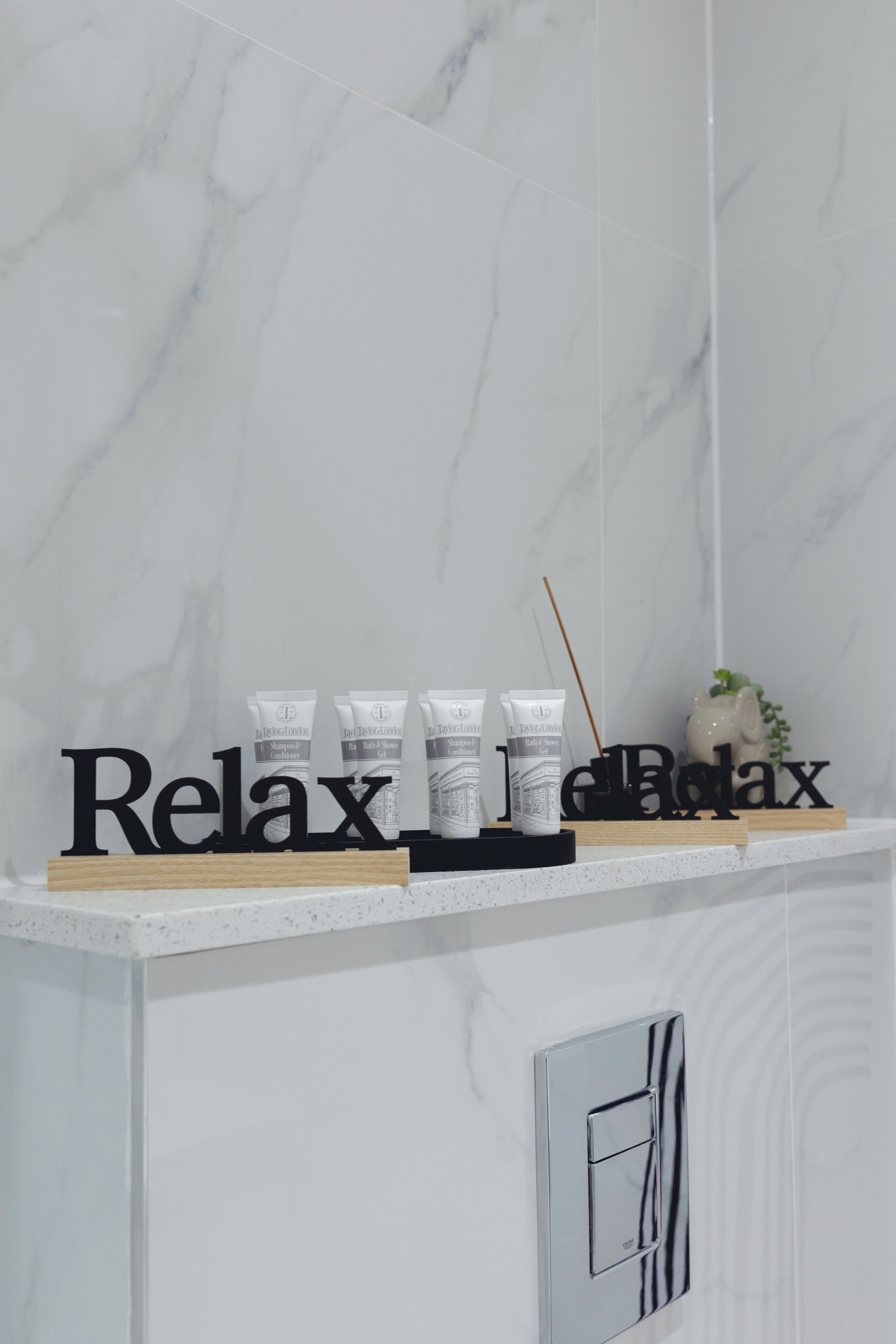 A bathroom with a white marble wall, a shelf with relaxation products, and a 'Relax' sign.