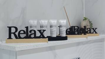 A bathroom with a white marble wall, a shelf with relaxation products, and a 'Relax' sign.