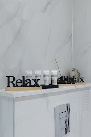 Une salle de bain avec un mur en marbre blanc, une étagère contenant des produits de relaxation et un panneau indiquant « Détendez-vous ».