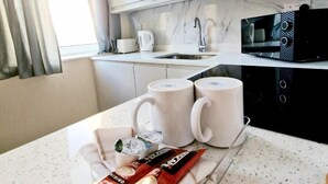 Une cuisine moderne avec des meubles blancs, un four à micro-ondes, une bouilloire et deux tasses posées sur le comptoir.