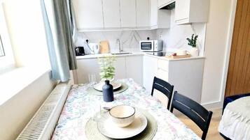A compact kitchen with white cabinets, a microwave, and a small countertop with a potted plant.