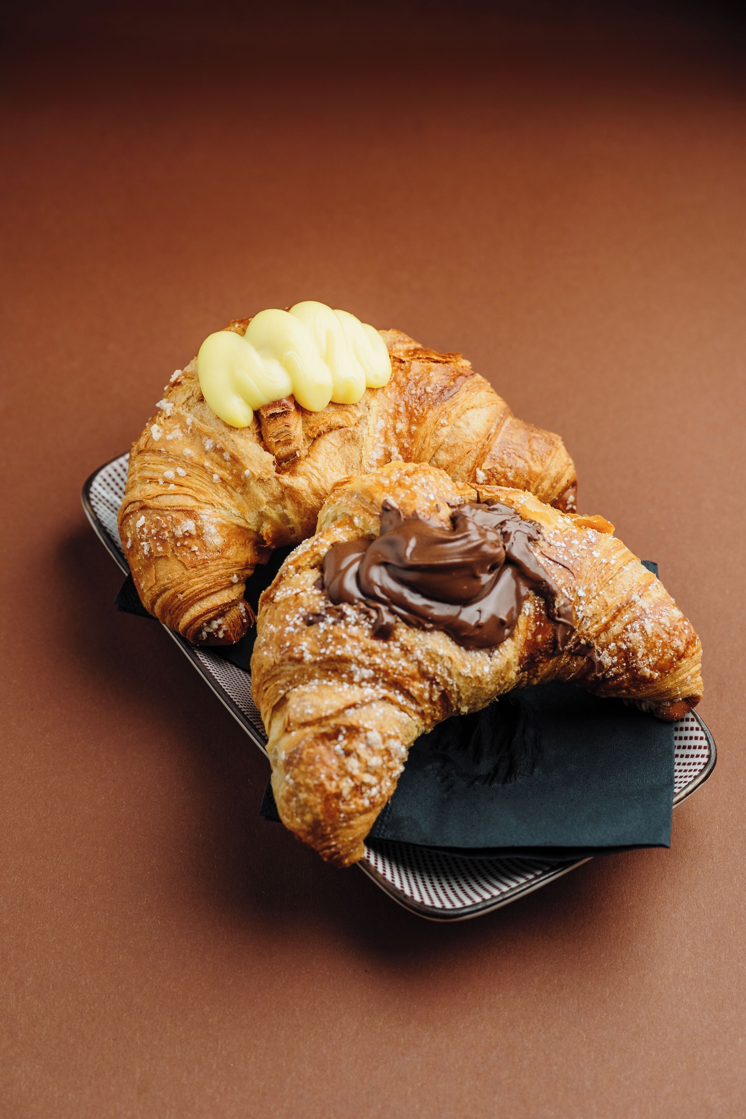 Two croissants, one with chocolate spread and the other with butter, on a tray.