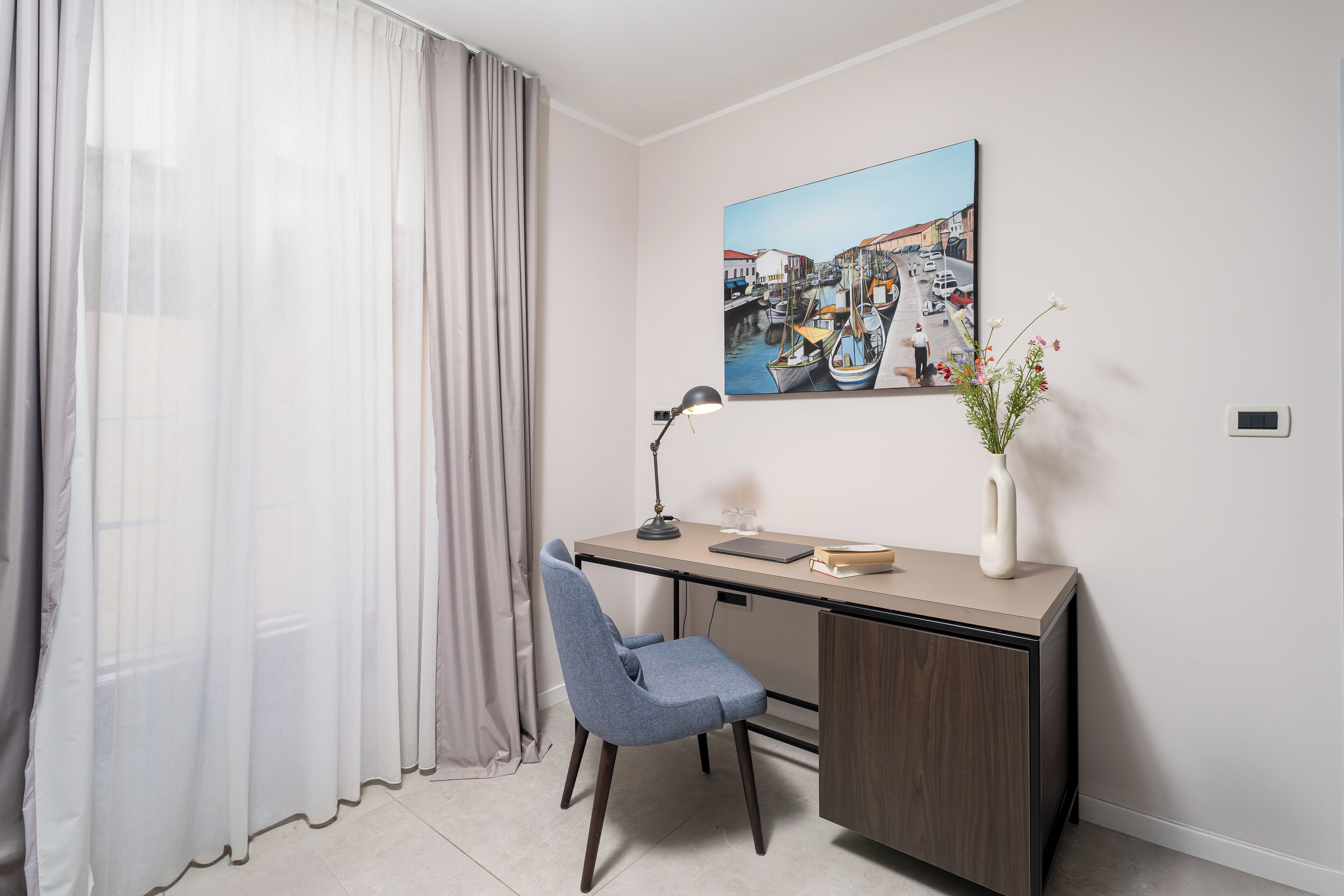 Une chambre moderne équipée d’un bureau, d’une chaise et d’un tableau représentant un paysage portuaire.