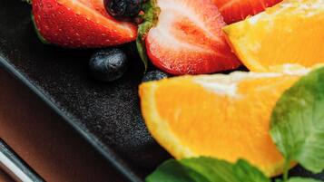 Un piatto nero rettangolare con frutta a fette, tra cui fragole, mirtilli e una fetta d'arancia, guarnito con foglie di menta.
