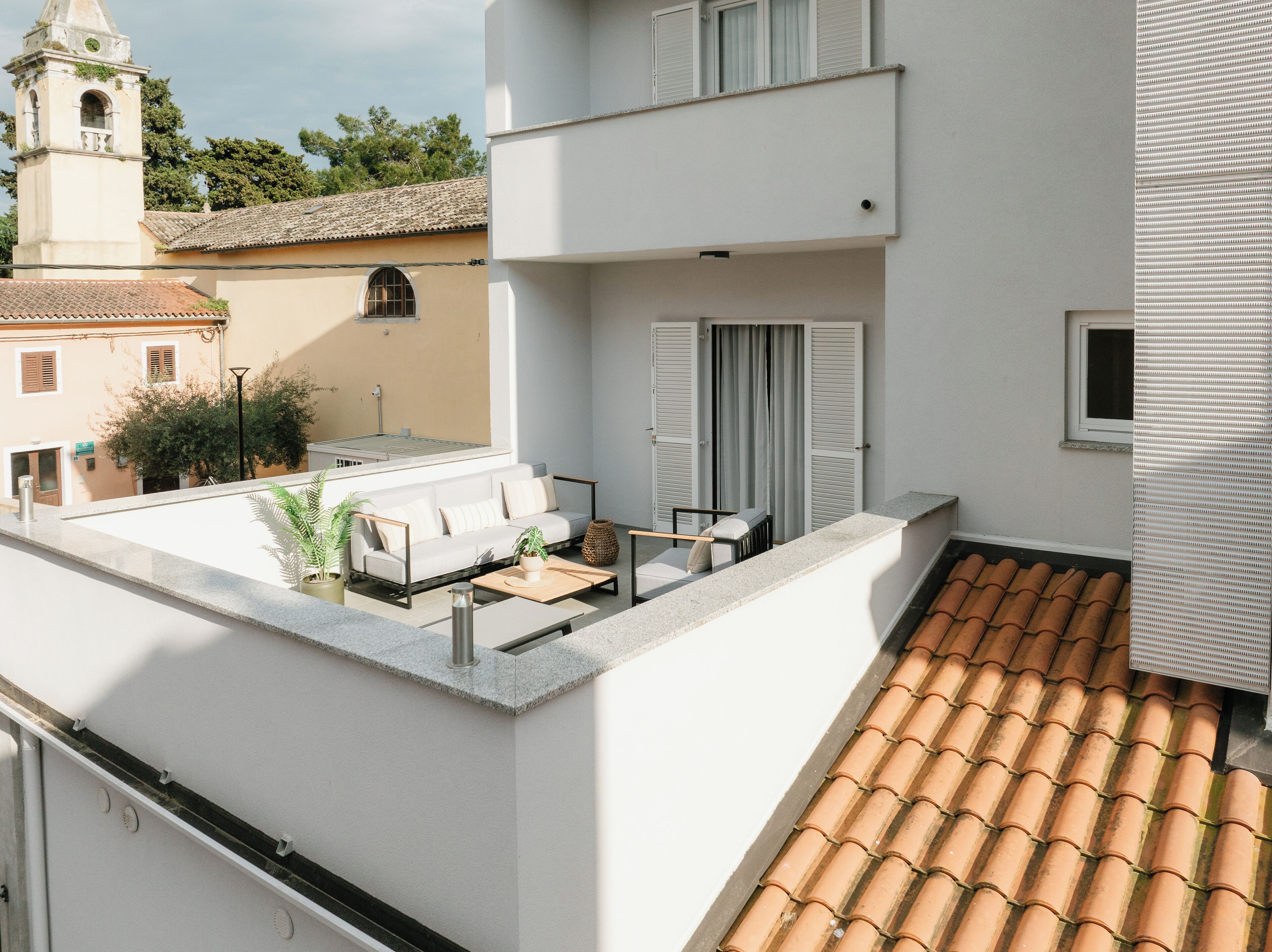 A rooftop terrace with a white sofa, a small table, and potted plants.