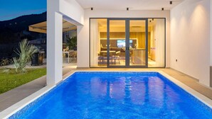 Une piscine extérieure moderne, dotée d’une structure en verre qui donne accès à un espace repas.