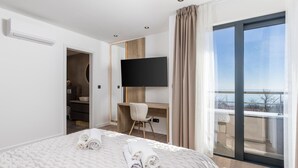Une chambre d’hôtel moderne dotée d’un grand lit, d’un téléviseur à écran plat fixé au mur, d’un bureau avec une chaise et d’un balcon offrant une vue agréable.