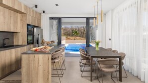 Une cuisine moderne dotée d’un îlot central, d’un coin repas avec vue sur la piscine et d’une grande porte-fenêtre coulissante.