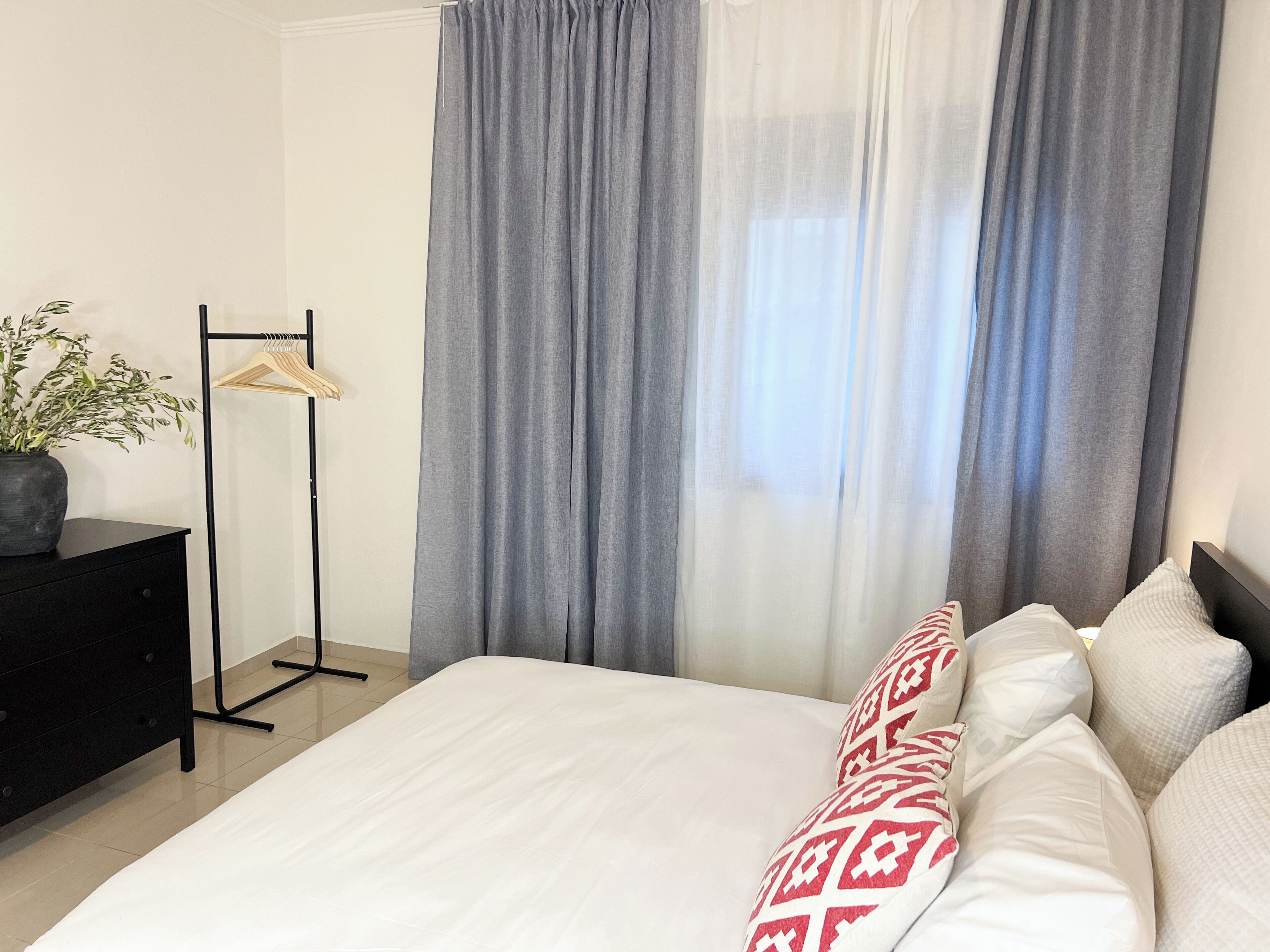 Een netjes ingerichte hotelkamer met een bed, nachtkastje, kaptafel en kledingrek.