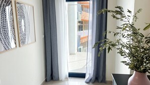 Ein Zimmer mit einer Schiebetür zum Balkon, einem Tisch mit einem Blumentopf und zwei gerahmten abstrakten Kunstwerken an der Wand.