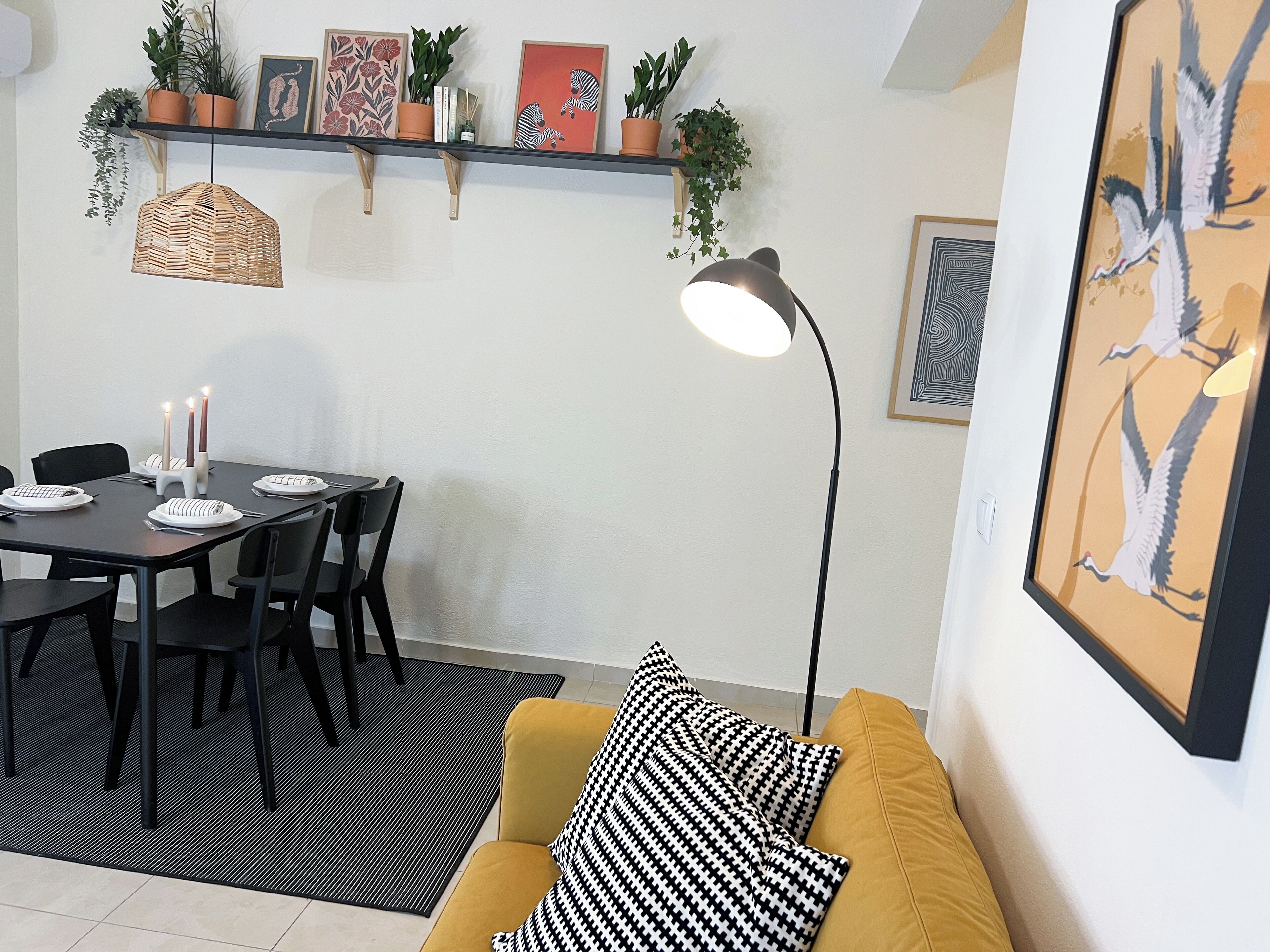 A dining area with a table set for four, a black and white patterned sofa, and a floor lamp.